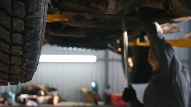 Mechanic in car service checks the auto's bottom for luxury SUV - slider shot