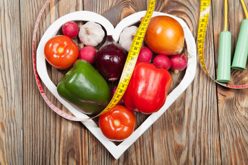 Sport and diet. Vegetables, dumbbells  centimeter. Peppers, tomatoes, garlic, onions,  radishes in the heart on rustic background