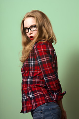 beautiful girl posing on a green background. Blonde girl in a plaid shirt and jeans. Girl in glasses with red lips and red nail polish. artistic portrait