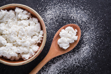 Cottage cheese in the dish and wooden spoon on the dark background in the kitchen. Tasty meal....