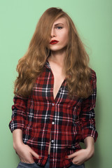 beautiful girl posing on a green background. Blonde girl in a plaid shirt and jeans. Girl with red lips and red nail polish. artistic portrait