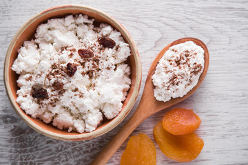 Cottage cheese in the dish with raisins on the wooden table in the kitchen. Tasty, sweet meal with apricots. Healthy eating and lifestyle.