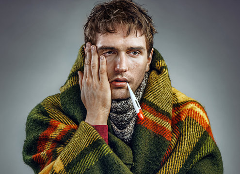 Ill young man with a thermometer in his mouth wrapped in plaid. Healthcare concept