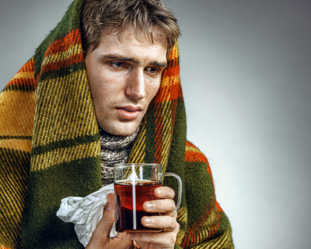 Ill Man covered with plaid blanket with hot tea. Sick man suffering cold and winter flu virus. Health care concept