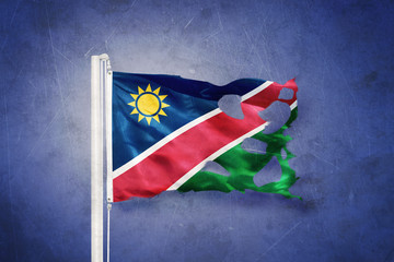 Torn flag of Namibia flying against grunge background