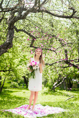 Gentle happy brunette woman with bouquet of peonies in among the trees  a sunny day