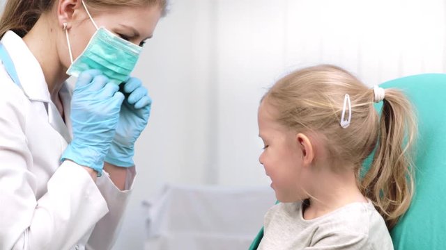 Female dentist putting on medical mask and starting examination of child teeth. Dental care concept. 
