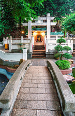 Fototapeta premium A small Buddhist temple with landscaped garden near 10000 Buddhas Monastery in Sha Tin, Hong Kong. Vertical view with stone bridge and trees