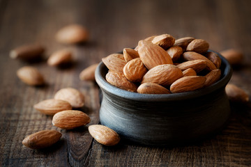 Almonds in a black bowl against dark rustic wooden background