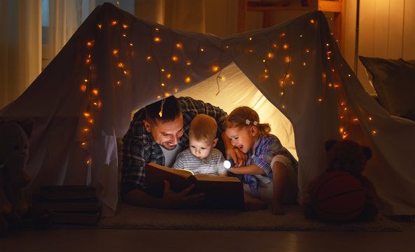 happy family father and children reading a book  in  tent at hom