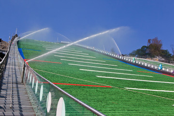 Green plastic coating of a ski jump hill is under summer maintenance with flushing water. Watering system at work