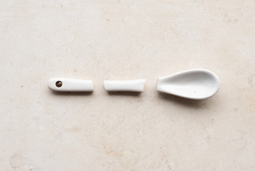 High angle view of broken white ceramic spoon on neutral limestone background - fragility concept