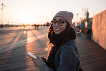 Portrait of a smiling pretty girl in eyeglasses using mobile