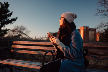 Smiling young woman in coat holding mobile phone