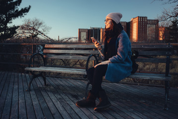 Young attractive girl in warm clothes holding mobile phone