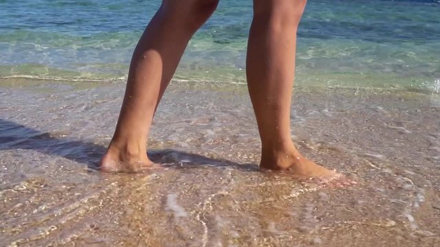 Female feet go on the sandy beach by the surf. Slow motion 100 fps.