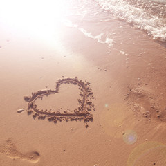Single love heart sign hand drawn on sunny sandy beach ground.