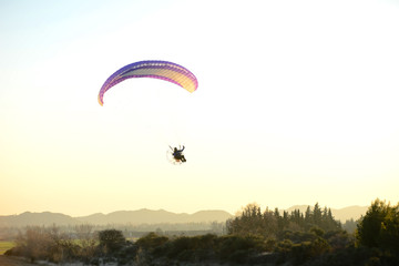 paramotor glider flying in the sky over beautiful countryside field landscape at sunset