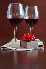 Two glasses of wine on a wooden table. Brown box with a bow.