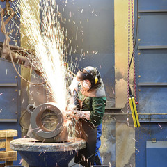 Industriearbeiter bearbeitet/ schleift Bauteil aus Metall mit einer Flex
