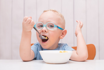 Happy baby boy wearing glasses sitting at the table and eating
