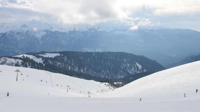 Group of people ride ski and snowboards by snow slope, view from peak of the mountain