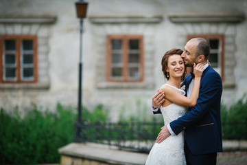 Naklejka premium Bride crosses her hands on groom's neck while they kiss on backy