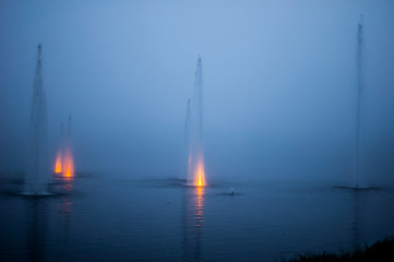 Mysterious fountain in a natural lake in a foggy night with colored jets