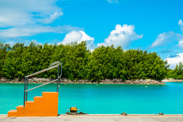 Tropical island jetty with orange boarding ladder and aquamarine sea on background