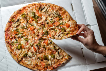 Pizza with jalapeno peppers. In the hand a slice of pizza
