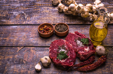 Raw Beef Steak, salt, pepper, garlic, rosemary  on the wooden board, background.