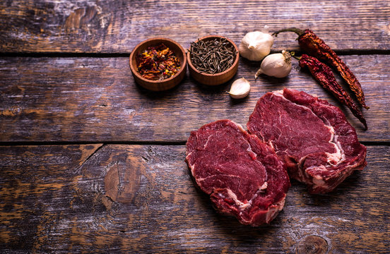 Raw Beef Steak, salt, pepper, garlic, rosemary  on the wooden board, background.
