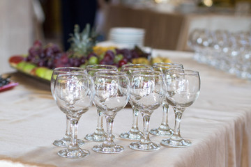 Empty wineglasses stand on beige table with fruits on dishes