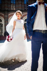 Wind blows bride's veil while she stands behind a groom on stone