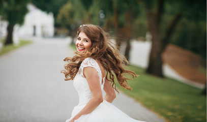 Cheerful bride with long dark blonde hair whirls on path in park