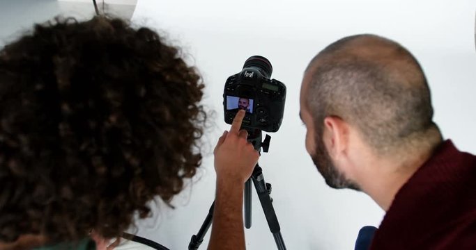 Photographer showing photos to fashion model during photo-shoot in studio 4k
