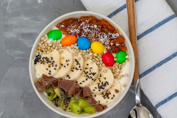 Breakfast smoothie bowl topped with chocolate, fruit, candy and banana. Love for a healthy vegan food concept