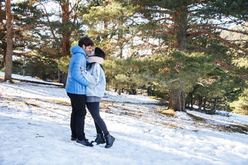 Fototapeta na wymiar Young couple, boyfriend and girlfriend kissing in the mountains on a snowy day. They are on a date traveling to the snowy forest. 