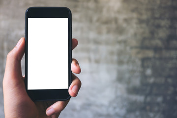 Mockup image of hand holding black mobile phone with blank white screen on concrete polishing wall background 