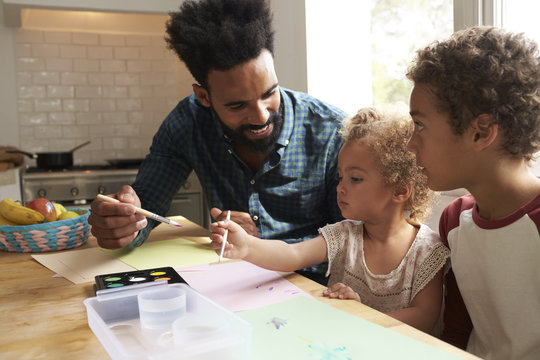 Children And Father Painting Picture On Kitchen Table