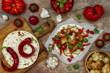 Spicy veggies tacos with roasted cauliflower,  zucchini and tomato salsa on rustic wooden cutting board. Preparing healthy lunch vegetarian snack. Top view, overhead, flat lay