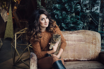 Fototapeta na wymiar beautiful smiling brunette girl with cat in her hands, sitting on sofa