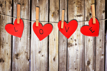 Four paper hearts with the word LOVE hanging on string on wooden background