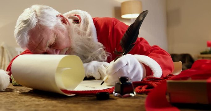 Santa Claus sleeping at desk while writing a letter with a quill during christmas time at home 4k