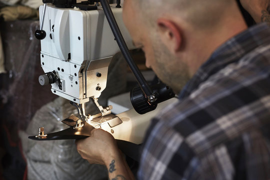 A man using an industrial sewing machine, stitching leather handmade goods. 