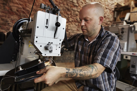A leather worker, craftsman using an industrial sewing machine on leather material, making a bag. 