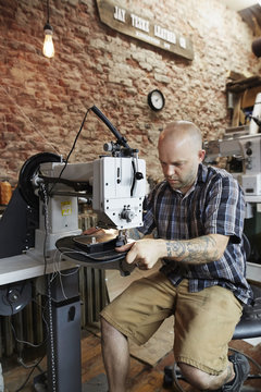 A leather worker, craftsman using an industrial sewing machine on leather material, making a bag. 