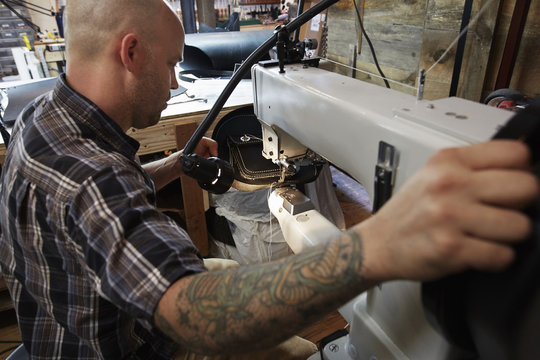 A leather worker, craftsman using an industrial sewing machine on leather material, making a bag. 