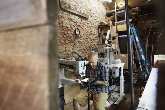 A leather worker, craftsman using an industrial sewing machine on leather material ion his workshop.