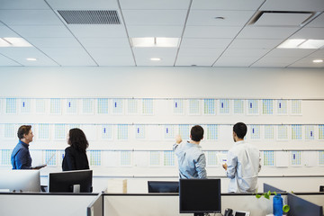 A woman and three men standing in an office looking at a display on a wall, seen from behind.